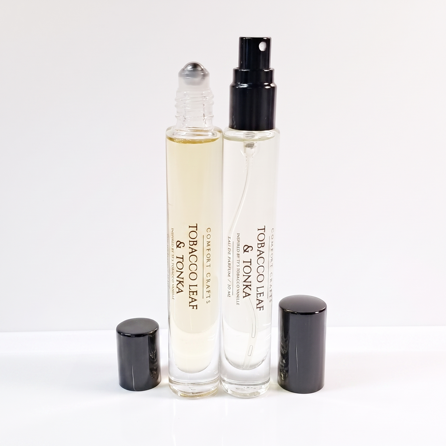 Two clear glass rollerball and spray perfume bottles with black caps, labeled Tobacco Leaf & Tonka by Comfort Crafts, on a clean white background.