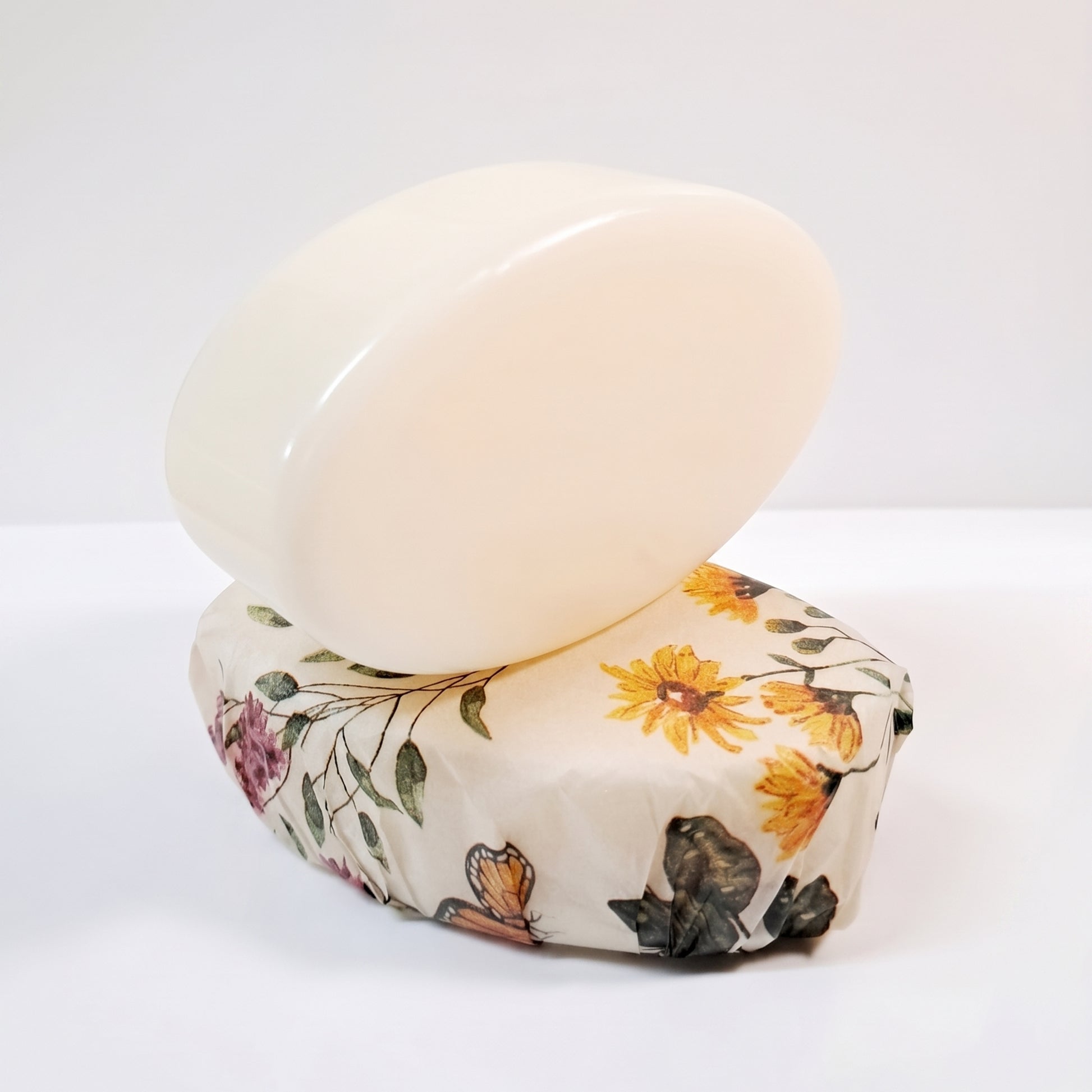 A translucent oval soap bar with a smooth glossy finish, resting on top of a small fabric-wrapped bar of soap featuring a yellow and pink floral pattern.